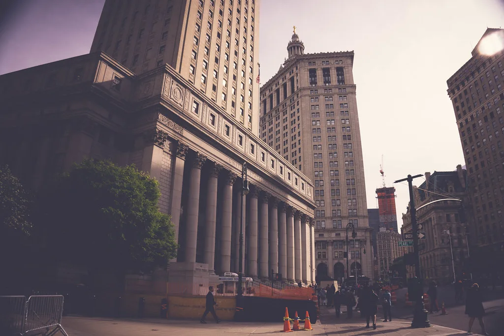 Palazzo neoclassico con colonnato e torri in mattone tra grattacieli nel distretto finanziario di Manhattan.