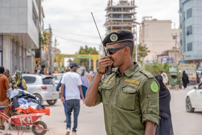 Ufficiale militare in uniforme verde parla via radio in una strada affollata di una città somala.
