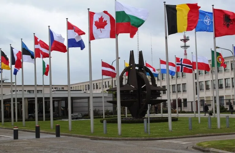 Bandiere di paesi NATO e partner sventolano intorno al simbolo dell'Alleanza davanti al quartier generale.