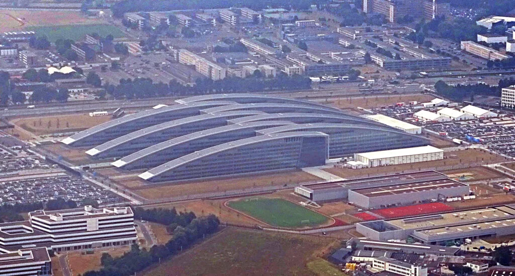 Complesso industriale moderno con edifici curvilinei e campi sportivi visti dall'alto in area urbana.