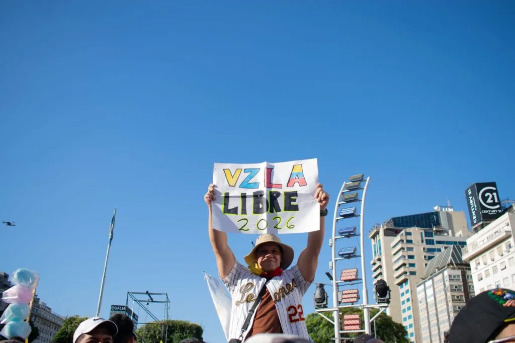Manifestante solleva un cartello con la scritta 'VZLA Libre 2026' durante una protesta in una piazza urbana.