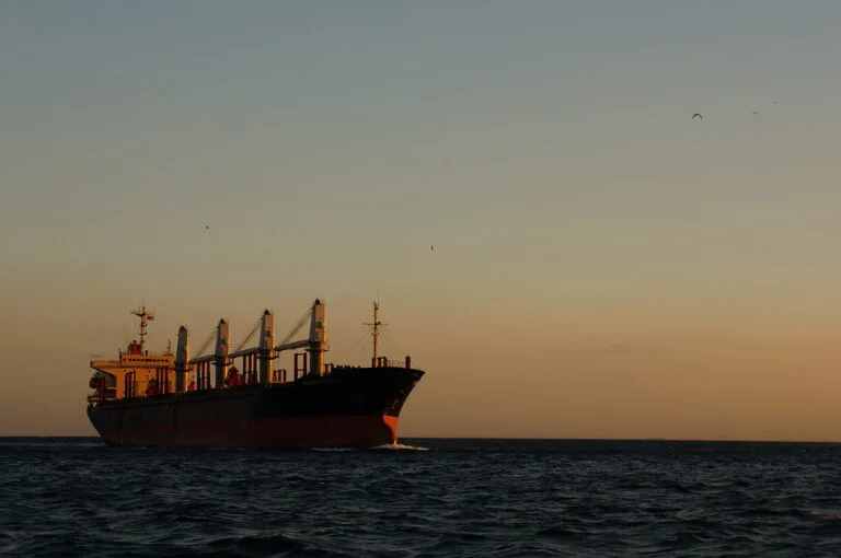 Petroliera carica di container in navigazione al tramonto su acque calme.
