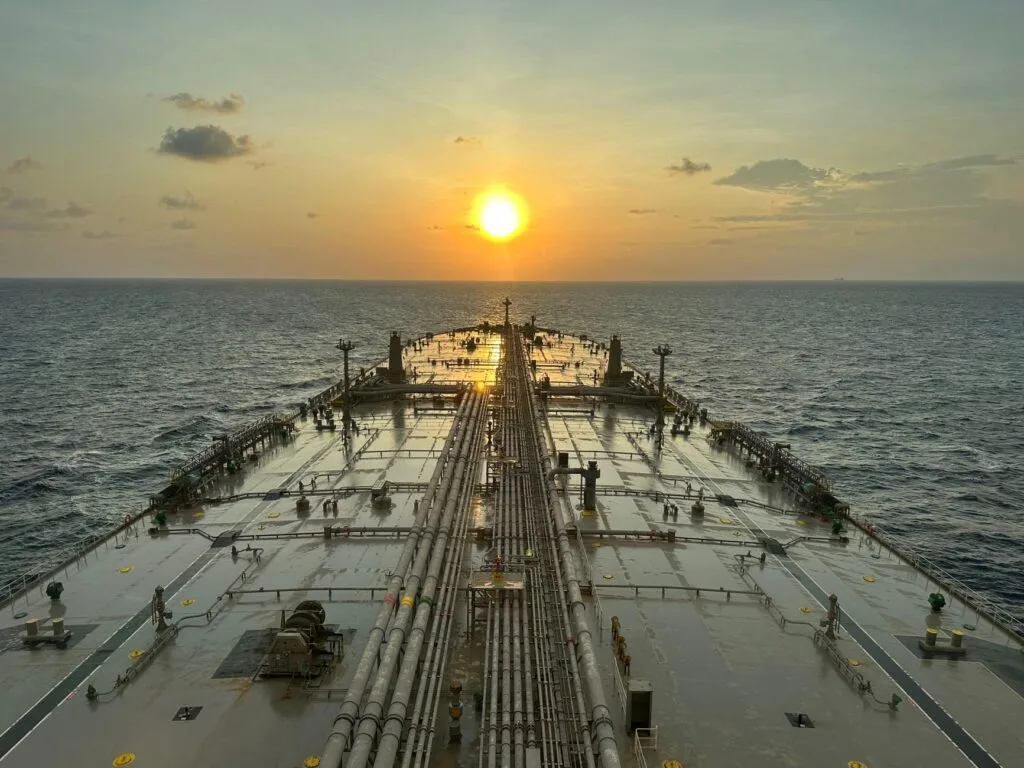 Petroliera nel Golfo Persico al tramonto, con il ponte di carico visibile dall'alto e il sole sull'orizzonte.
