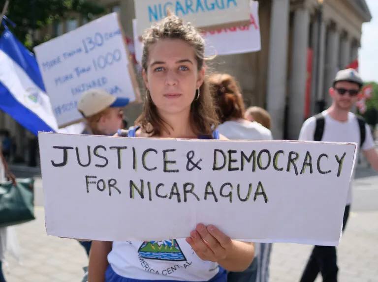 Una manifestante regge un cartello con scritto "Justice & Democracy for Nicaragua" durante una protesta in strada, con…