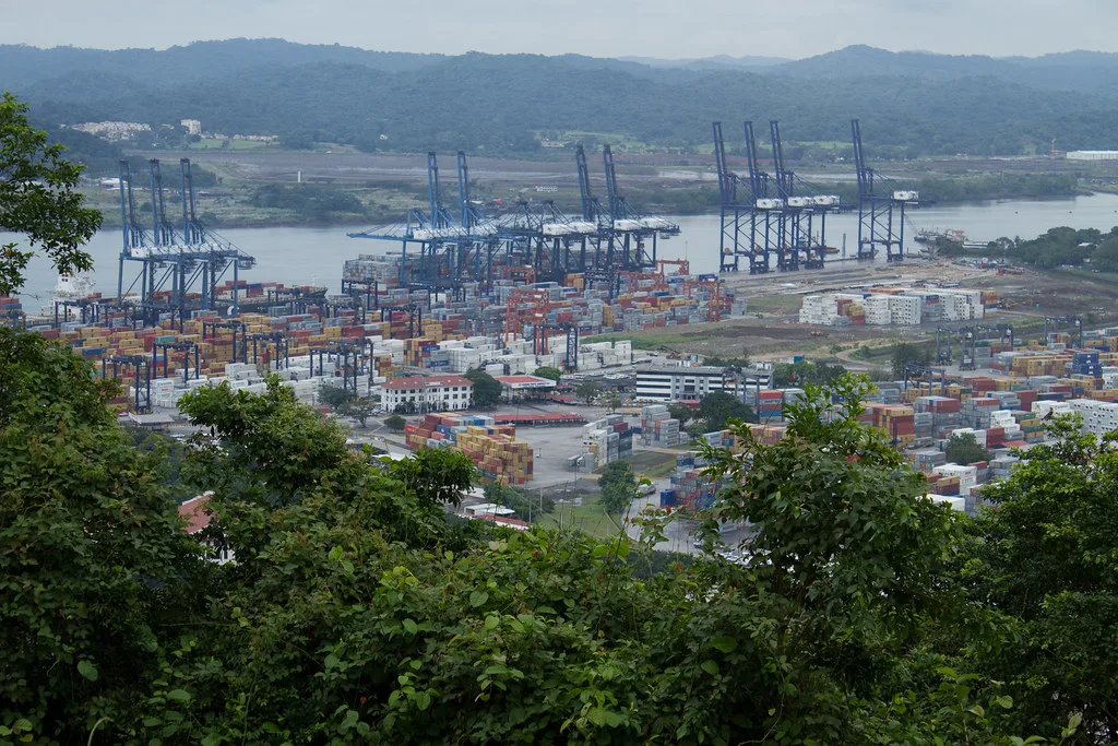 Porto container di Panama con gru e container colorati affacciato su canale navigabile tra colline boscose.