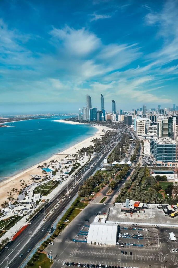 Vista aerea di Abu Dhabi con grattacieli moderni, spiaggia bianca e mare azzurro cristallino sotto cielo sereno.