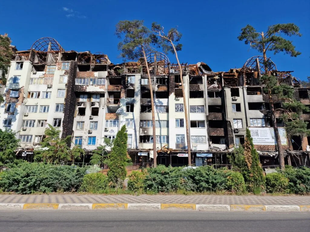Edificio residenziale devastato con facciate bruciate, tetti crollati e finestre vuote, circondato da vegetazione e alberi.