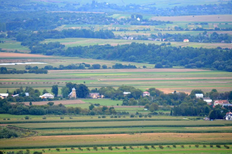 Paesaggio agricolo ondulato con campi coltivati, boschi e piccoli insediamenti rurali sparsi tra le colline.