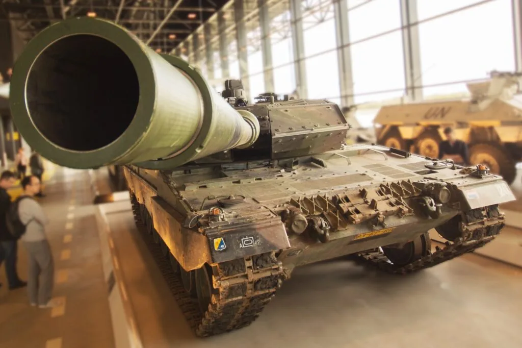 Carro armato esposto in un hangar con ampio cannone principale e carrello cingolato, fotografato da vicino.