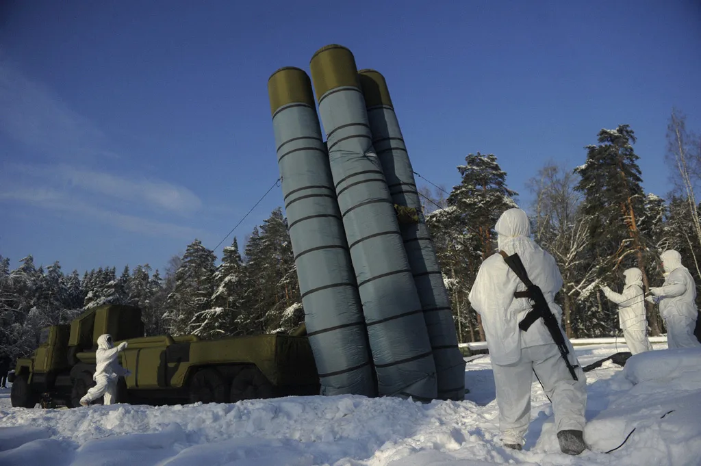 Militari in uniforme bianca invernale accanto a un sistema missilistico S-300 in neve, in una foresta di conifere.