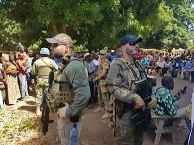 Soldati in uniforme militare russa circondati da civili africani in una zona all'aperto con vegetazione.
