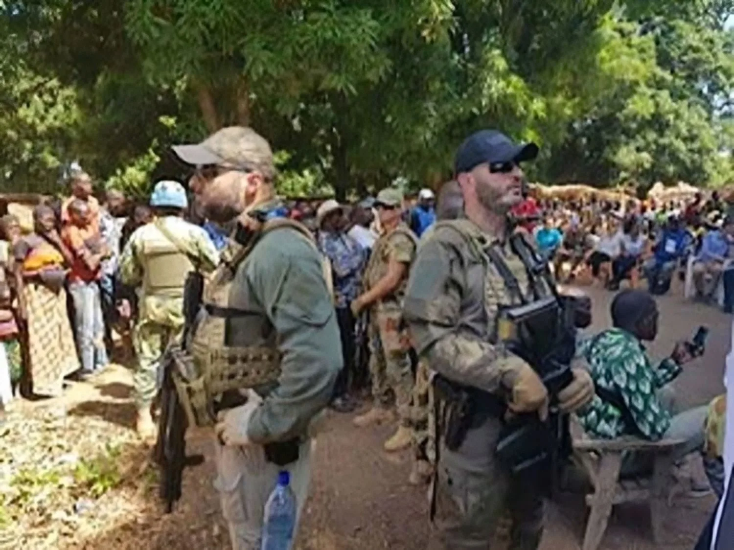 Soldati in uniforme militare russa circondati da civili africani in una zona all'aperto con vegetazione.