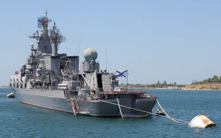 Nave militare russa in rada con sistema radar e torrette di fuoco, ormeggiata davanti a costa sabbiosa.