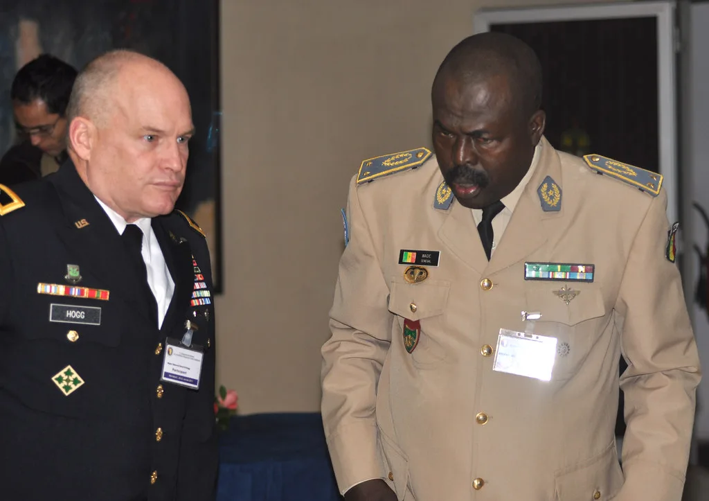 Due ufficiali militari in uniforme conversano: uno americano in blu scuro e uno africano in divisa sabbia con gradi elevati.