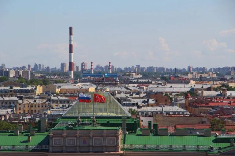 Skyline di San Pietroburgo con camini industriali, bandiere russe e un edificio verde in primo piano.
