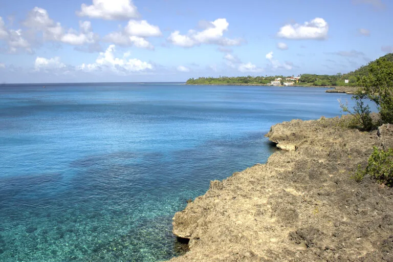 Scogliera calcarea affacciata su acque turchesi con vegetazione tropicale sullo sfondo.