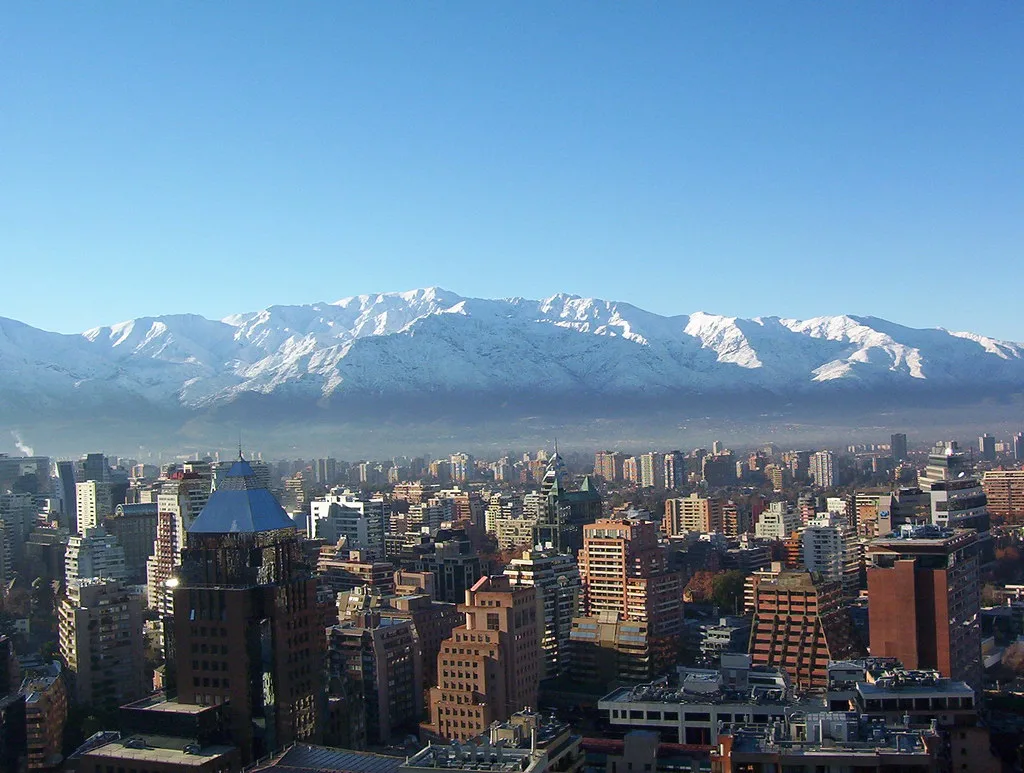 Skyline di Santiago del Cile con grattacieli e edifici residenziali sullo sfondo delle Ande innevate sotto cielo sereno.