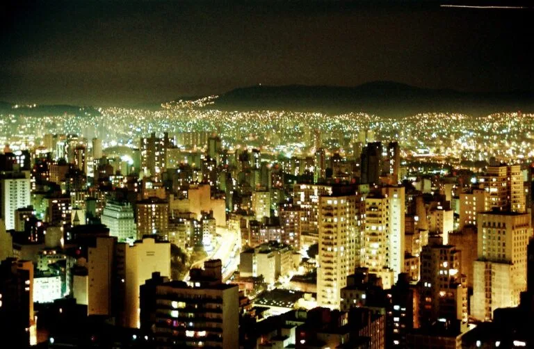 Skyline notturno di San Paolo con migliaia di luci sparse sulle colline e grattacieli illuminati in primo piano.