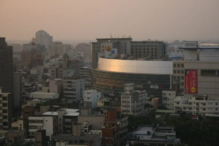Skyline urbana di Hsinchu con edifici moderni e un grande stadio illuminato al tramonto.