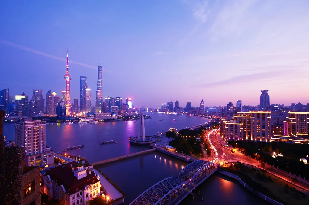 Skyline di Shanghai al tramonto con grattacieli illuminati riflessi nelle acque del fiume Huangpu.