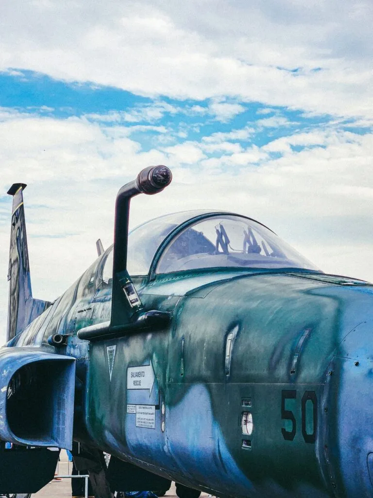 Aereo militare con fusoliera blu-verde e numero 50, fotografato contro un cielo nuvolato.