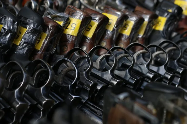 Revolver neri con grilletti esposti allineati su un supporto, con etichette gialle identificative sulle canne.