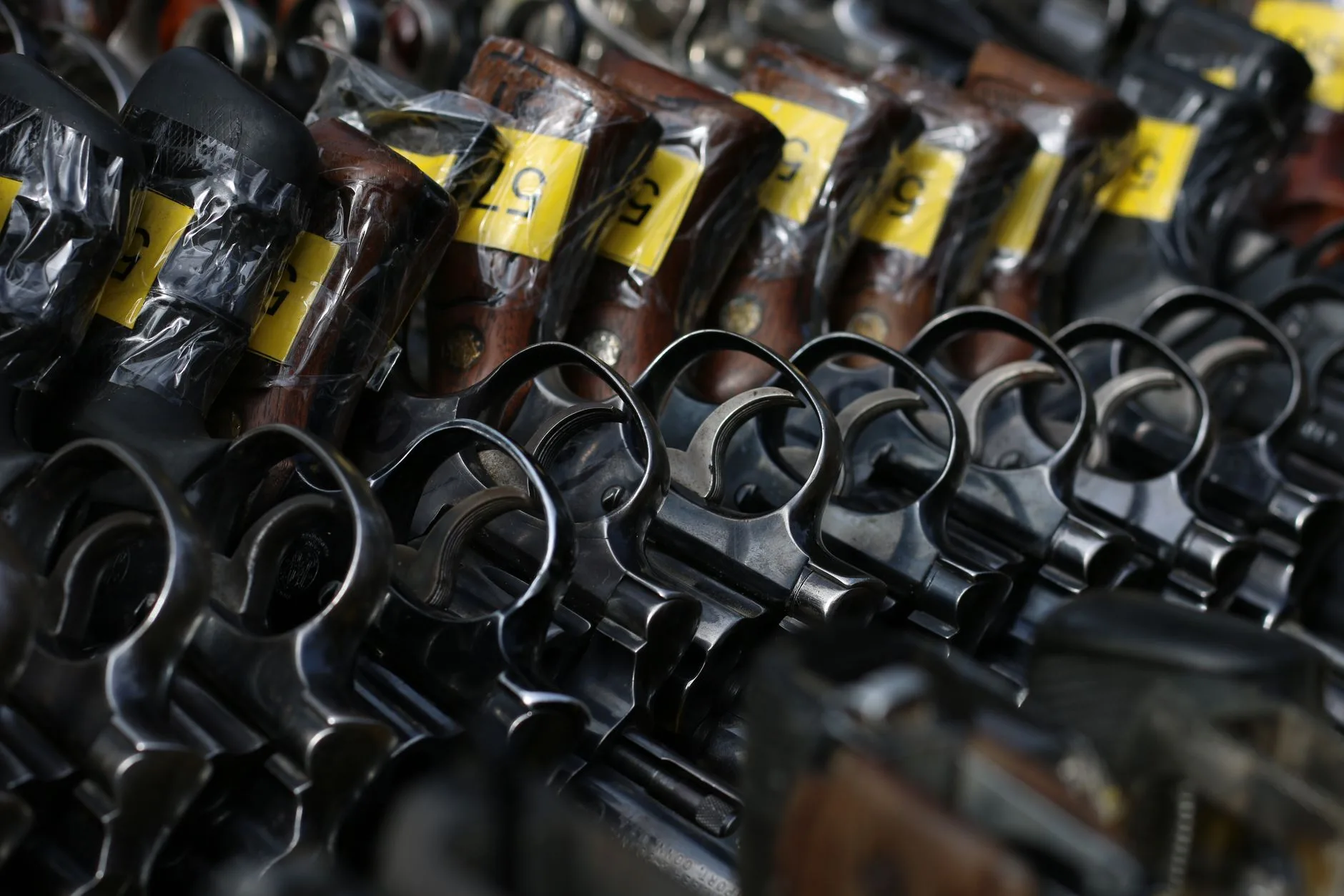 Revolver neri con grilletti esposti allineati su un supporto, con etichette gialle identificative sulle canne.