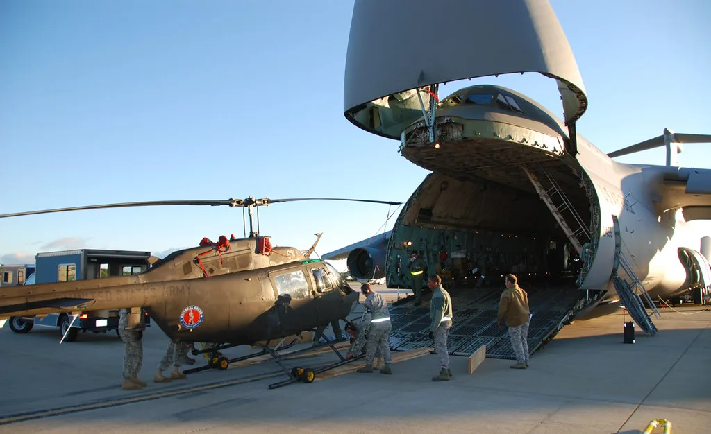 Elicottero militare caricato in un aereo cargo con personale in uniforme che supervisiona l'operazione.