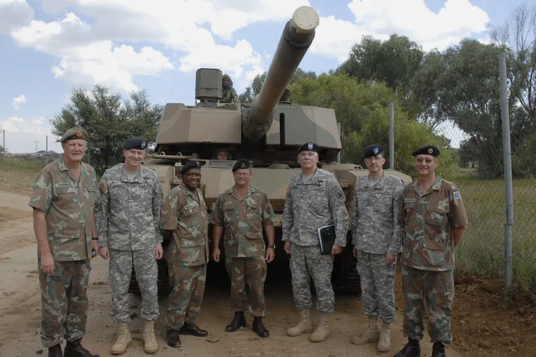 Sette militari in uniforme mimetica posano davanti a un carro armato in una base militare.