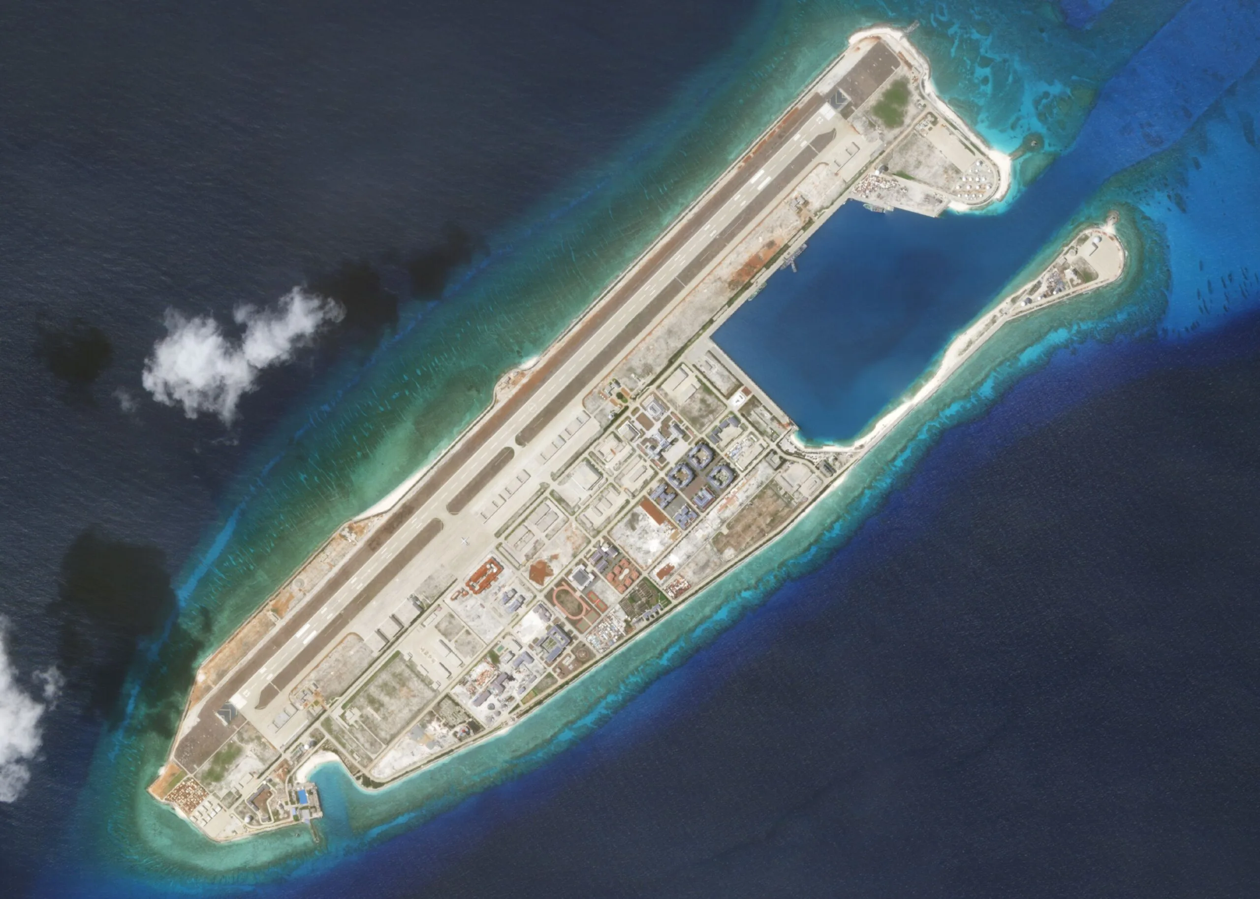 Isola artificiale con pista aeroportuale e strutture portuali circondata da acque blu.