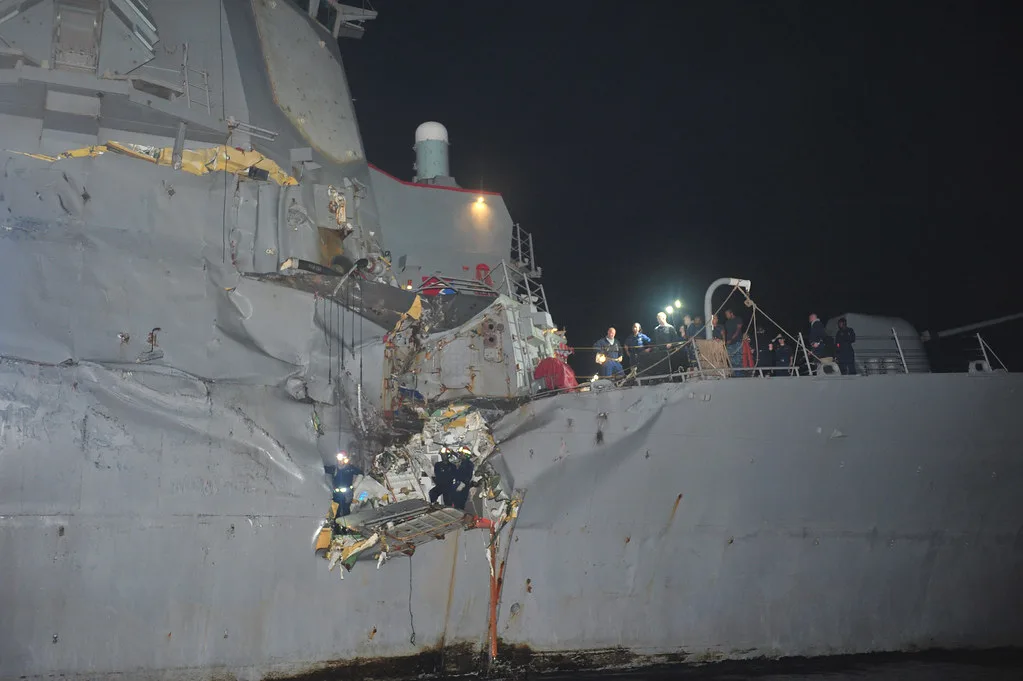Nave cargo illuminata di notte con danno visibile allo scafo e operazioni di ispezione in corso.