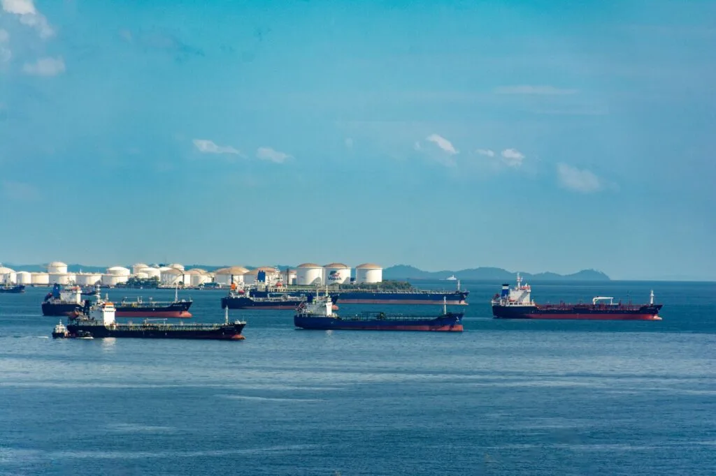 Petroliere e navi cargo ancorate in rada davanti a un terminale con serbatoi di stoccaggio in un porto costiero.