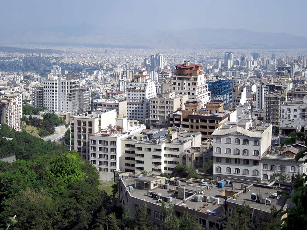 Veduta aerea di Teheran con edifici residenziali e commerciali distribuiti su un territorio ampio circondato da montagne.