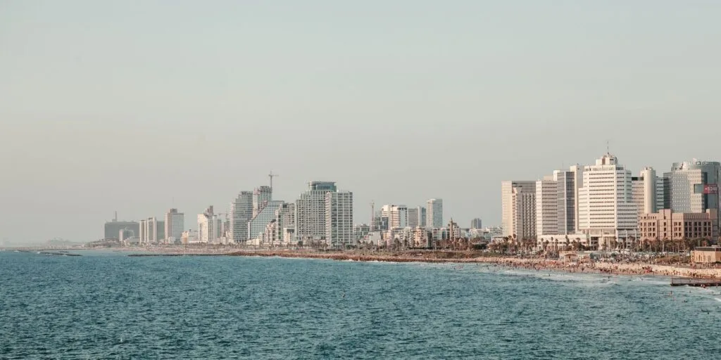 Skyline di grattacieli affacciata sul mare azzurro con spiaggia sabbiosa al tramonto.