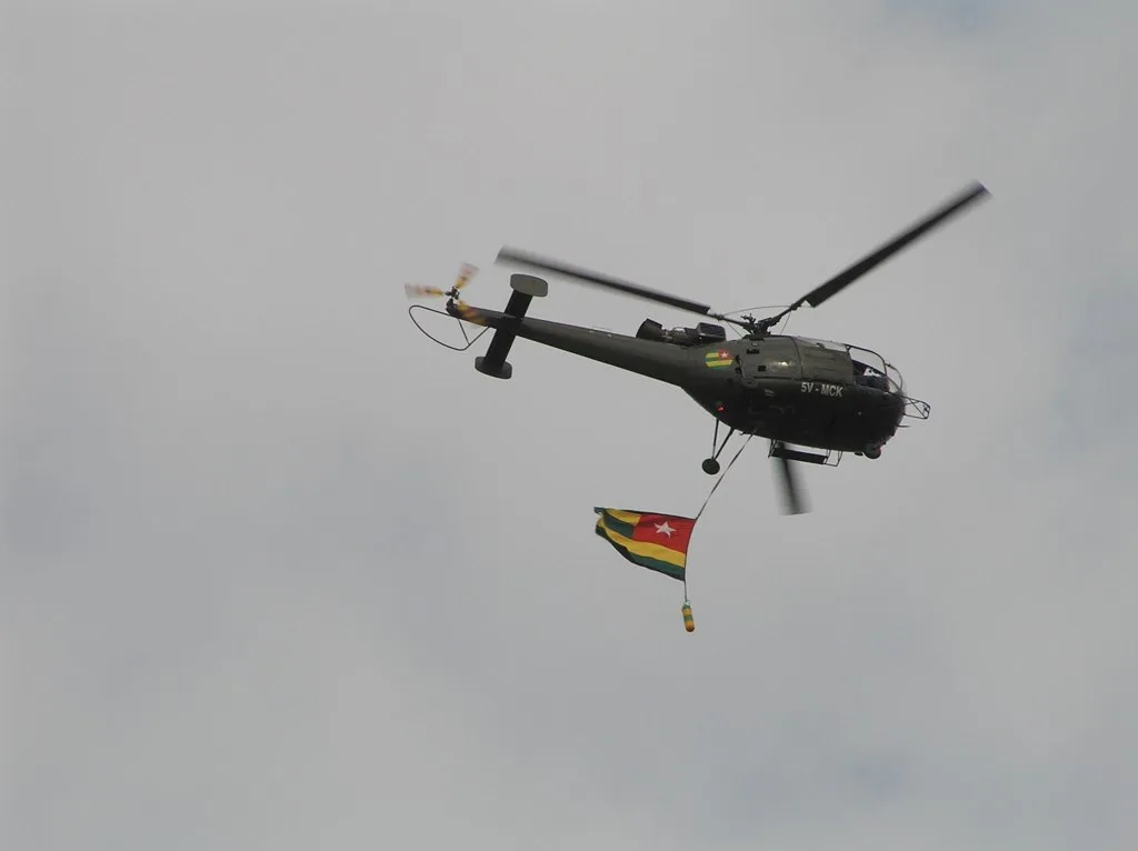 Elicottero militare in volo con bandiera togolese appesa sotto la fusoliera.