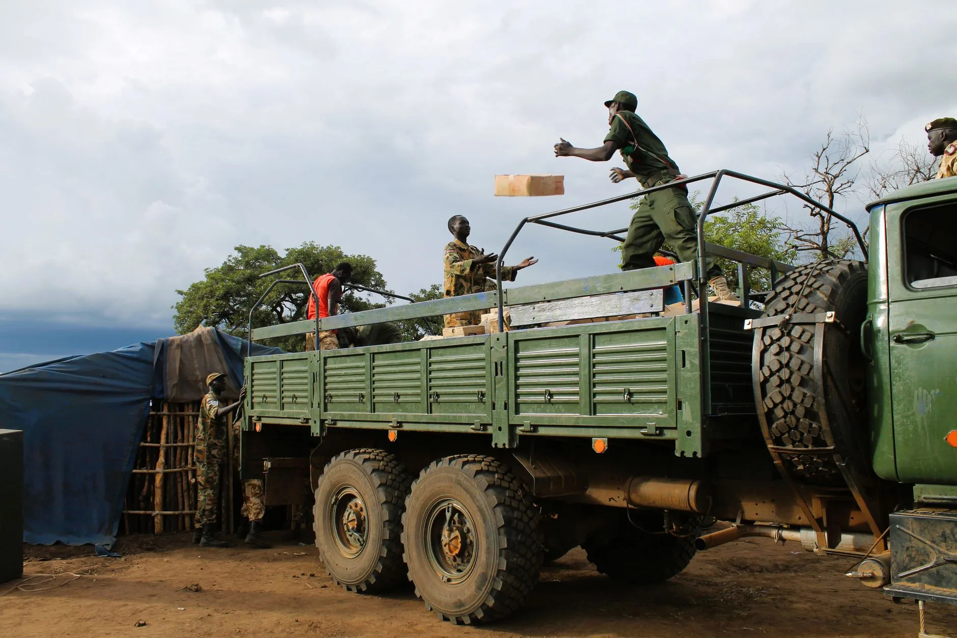 Soldati in uniforme caricano rifornimenti su un camion militare verde in un'area desertica.