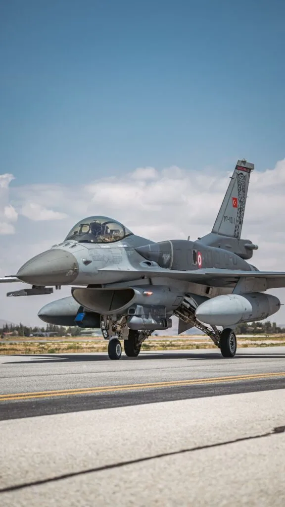 Un caccia F-16 con insegne turche parcheggiato sulla pista di un aeroporto con armamenti sottolari.