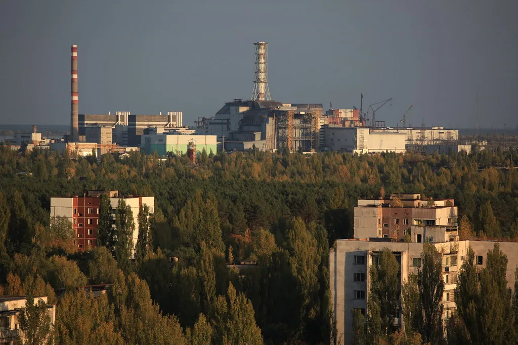 Complesso industriale con reattore nucleare tra foreste di conifere e edifici residenziali in primo piano.