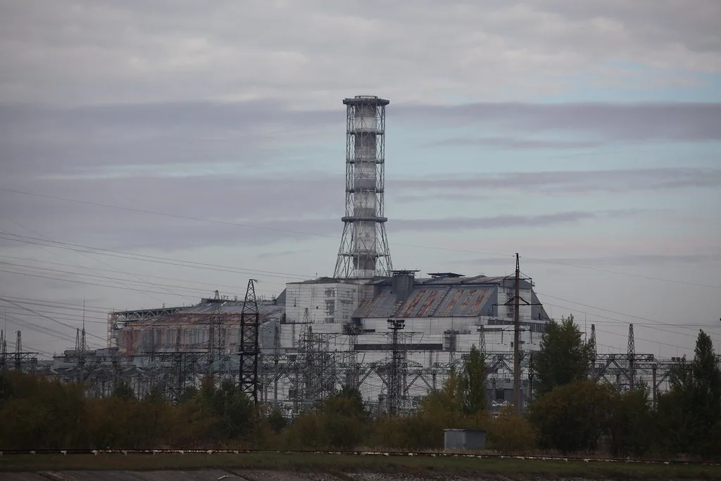 Centrale nucleare con caratteristico camino a torre circondato da strutture industriali e vegetazione spontanea.