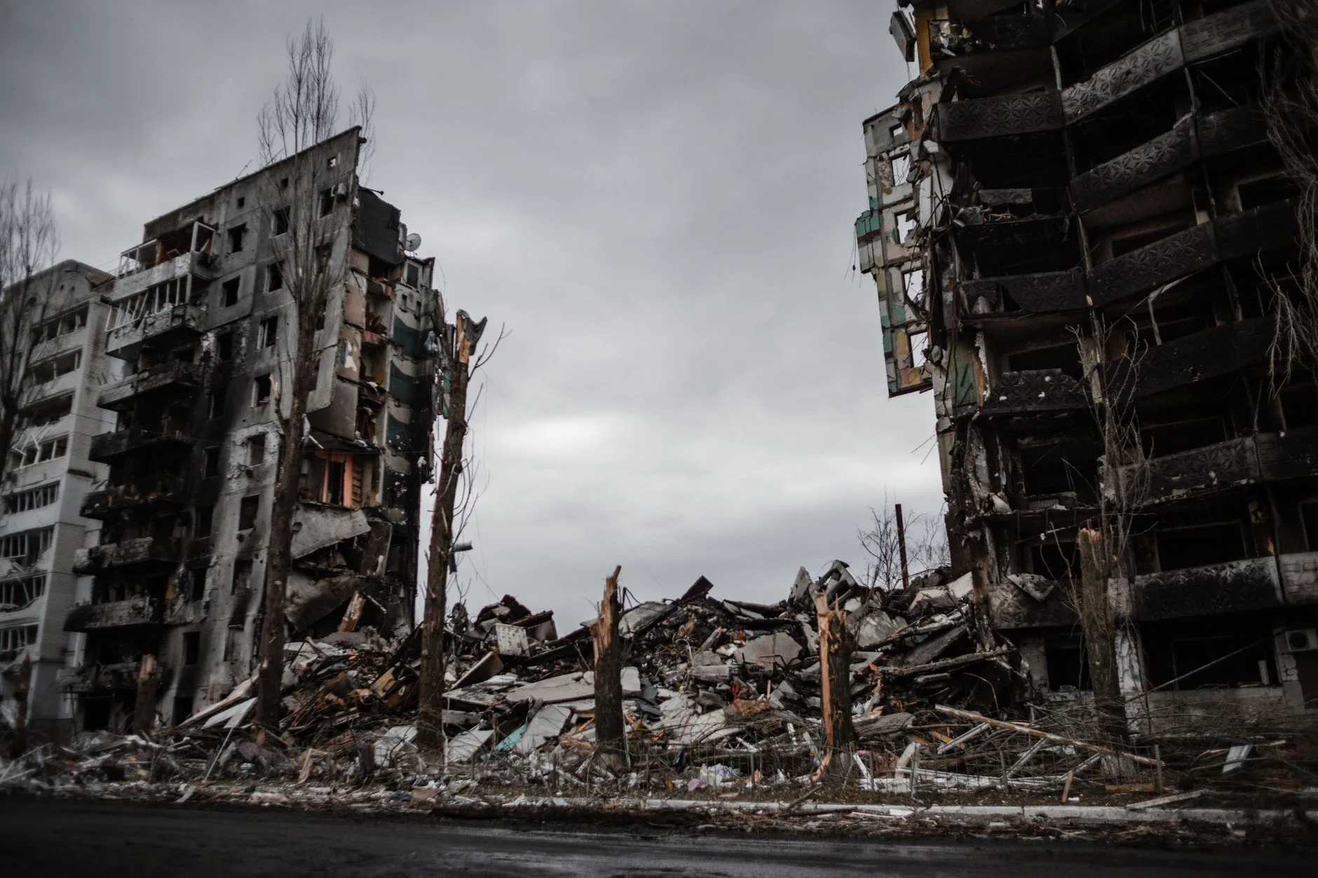 Edifici residenziali devastati dai bombardamenti, con facciate crollate e macerie sparse al suolo sotto un cielo nuvoloso.
