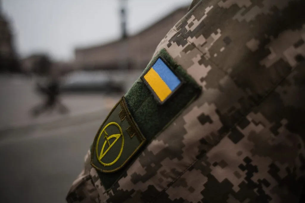 Bandiera ucraina e stemma militare cuciti su una divisa mimetica digitale.
