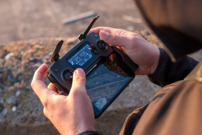 Mani che tengono il telecomando di un drone con schermo integrato durante un'operazione all'aperto.