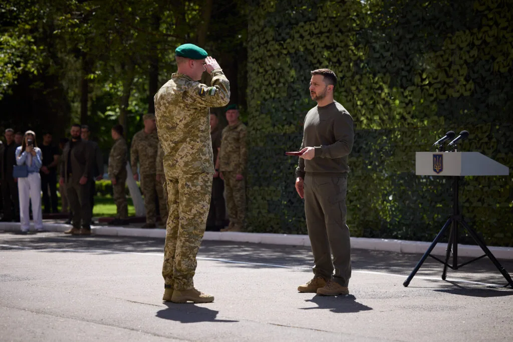 Ufficiale militare in uniforme mimetica riceve un riconoscimento durante una cerimonia ufficiale all'aperto.