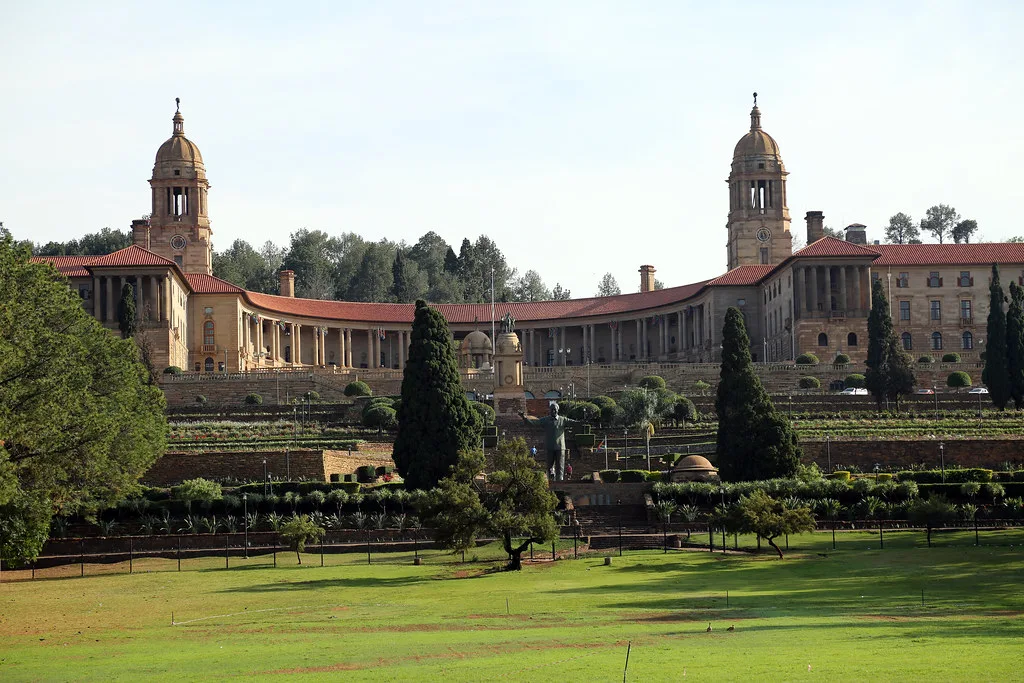 Edificio governativo in stile coloniale con due torri simmetriche, giardini formali e prato verde in primo piano.