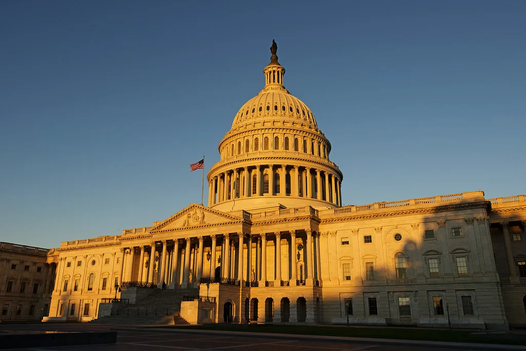Cupola dorata del Campidoglio americano illuminata al tramonto, con bandiera americana sulla sommità.