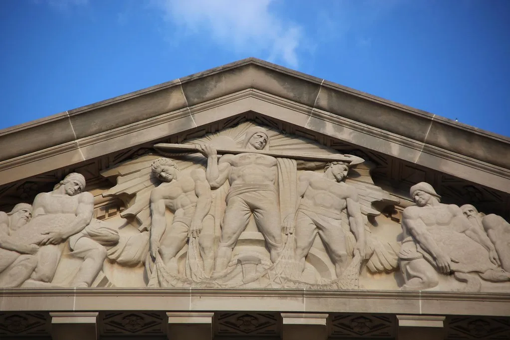 Frontone neoclassico in marmo con figure allegoriche scolpite, raffigurante il commercio e l'industria.