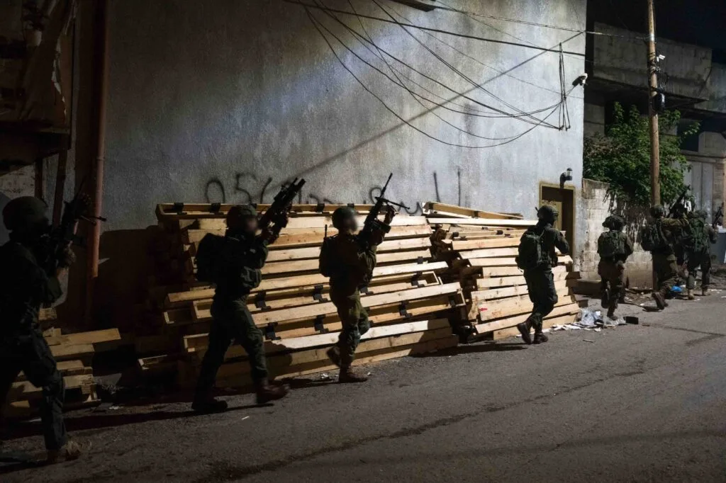 Soldati in uniforme nera posizionati dietro una barricata di legno in una strada urbana.