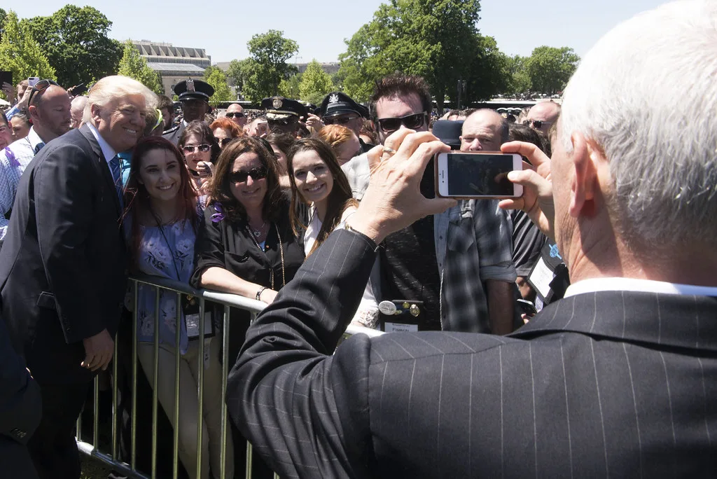 Persone in abiti formali si raccolgono attorno a dignitari mentre qualcuno fotografa con smartphone durante un evento…
