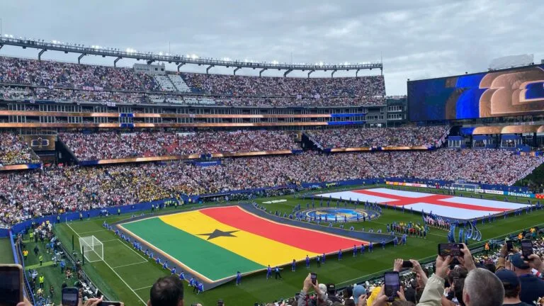 Stadio gremito durante una cerimonia pre-partita con bandiera tricolore spiegate sul campo.