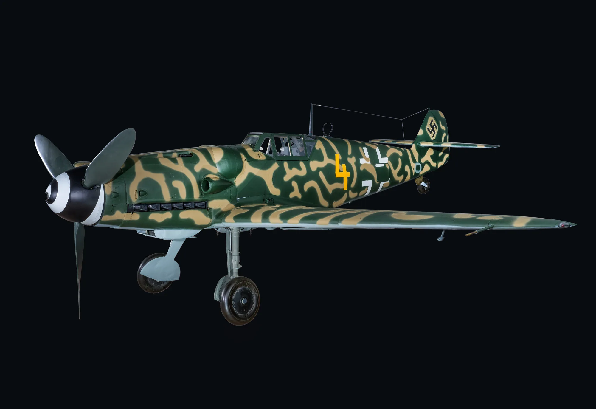 Aereo da caccia militare con mimetizzazione giallo-verde e croci nere, fotografato su sfondo nero in posizione laterale.
